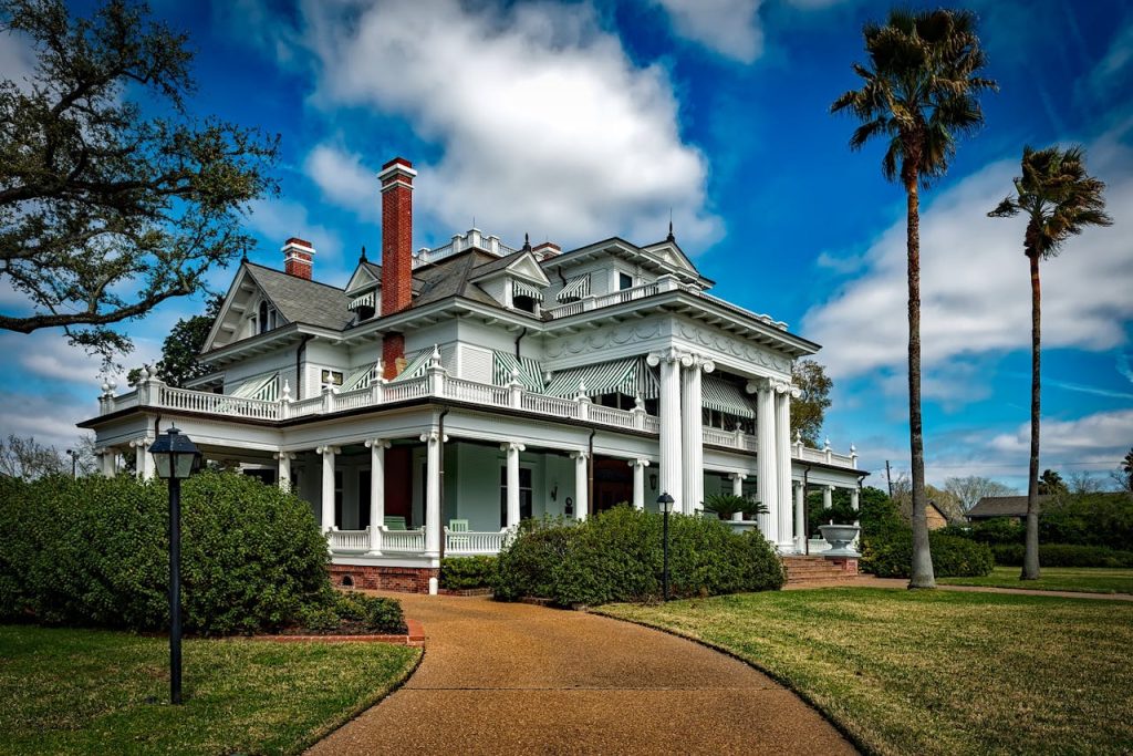 Beautiful white mansion with pillars and palm trees under a bright blue sky.